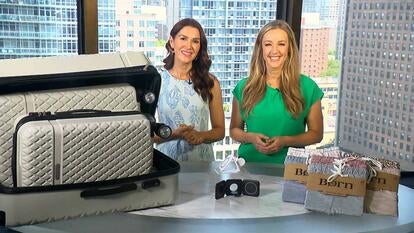 Two women standing behind a table displaying a luggage set, charging pad, and joggers