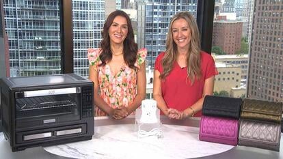 Two women standing behind a table displaying an oven, a charging station, and crossbody bags