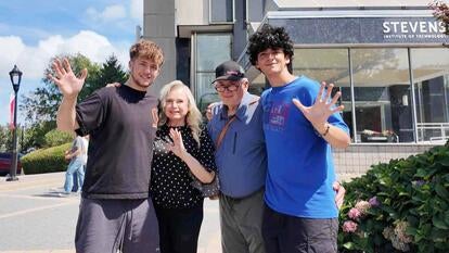 Family photo of two young adult men waiving next to an older man and woman 