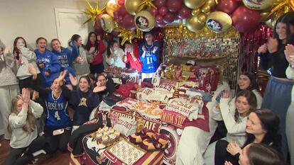 Bedroom full of young people cheering next to a bed covered in college paraphenalia 