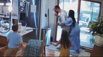 Pregnant woman giving husband Heimlich maneuver in their home, as their two children look on