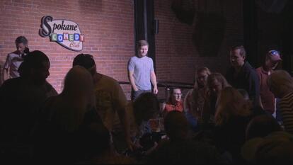 Comedian Drew Lynch watches from the stage as an audience member needs assistance