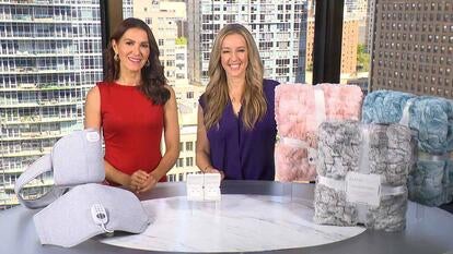 Two women standing behind a table displaying a Heat Wrap, Stud Earrings, Throw Blanket