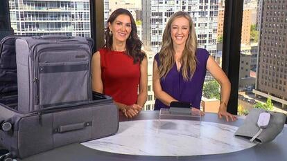 Two women standing behind a table displaying a Luggage Set, Wireless Charger with Clock, Heat Pad