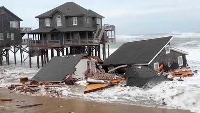 A collapsed home in the high tide as two houses on stilts stand in the background