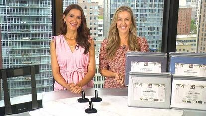Two women behind a table displaying a Scale, Diamond Muse Bracelet, Bibb Home Sheet Set