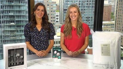 Two women standing behind a table displaying a Flatware Set, Locator Tags, Mattress Topper