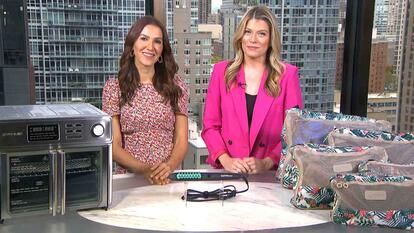 Two women standing behind a table displaying Kalorik Air Fryer, Dafni by Conair Hot Brush, Triforce Packing Cube Set