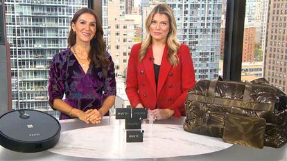 Two women standing behind a table displaying a Robot Vacuum, Power Banks, Duffel Bag
