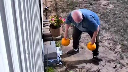 Man taking two small pumpkins off the front steps of a home