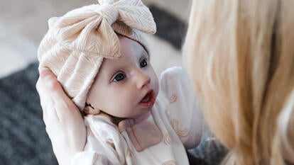 Image of baby Hazel, swaddled in white, looking up at person holding her