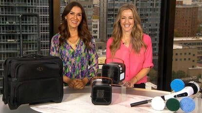 Two women standing behind a table displaying an Overnighter Bag, TheraMist Space Heaters, Electric Scrubber Brush