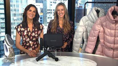 Two women standing behind a table displaying a Iron & Steamer, Tissue Massager, Puffer Jacket