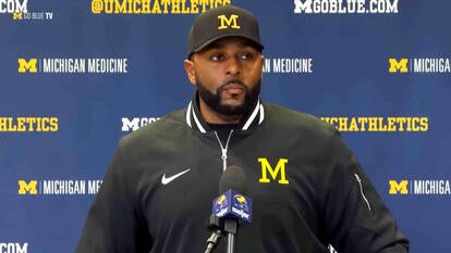 Coach Sherrone Moore being interviewed in front of a step-and-repeat