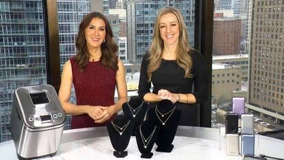 Two women standing behind a table displaying a Bread Maker, Necklace, Power Bank