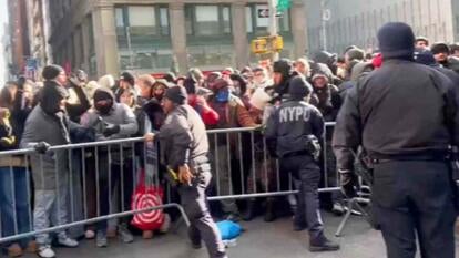 NYPD officers standing against a metal fence on the otherside of a large crowd of people