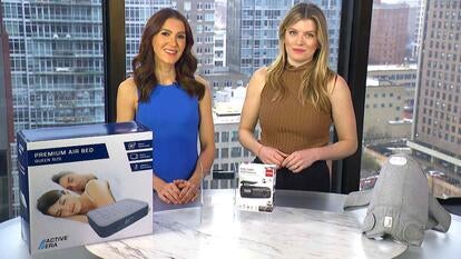 Two women standing behind a table displaying an Air Mattress, Dash Cam, Shoulder Wrap