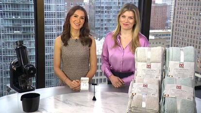 Two women standing behind a table displaying a Juicer, Earrings, Towel Set