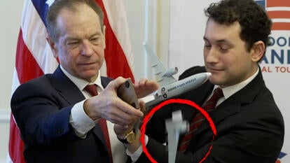 Two men holding a model of a plane as the wing falls off