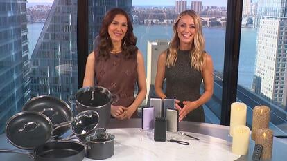Two women standing behind a table displaying a Cookware Set, Power Bank, Candles