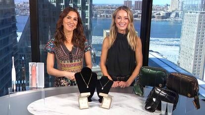 Two women standing behind a table displaying an Electric Toothbrush, Jewelry, Sling Bag