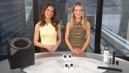 Two women standing behind a table displaying an Air Purifier, Security Cameras, Cordless Vacuum