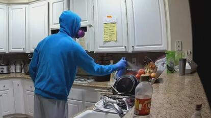 Man in blue hoodie and protective mask spraying bug spray in kitchen