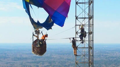 Colorful hot air balloon hanging from a cell phone tower as firefighters climb the tower ladder