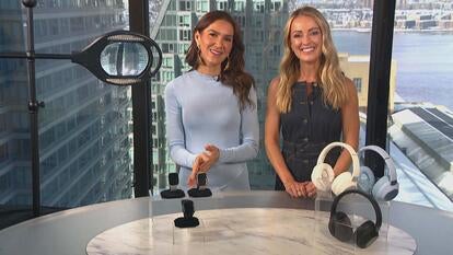 Two women standing behind a table displaying a Magnifier, Smartwatch, Wireless Headphones