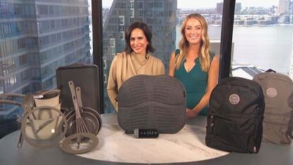 Two women standing behind a table displaying a Cookware Set, Stretch Mat, Backpacks