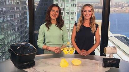 Two women standing behind a table displaying a Multi-Cooker, Egg Cooker, Steamer Iron
