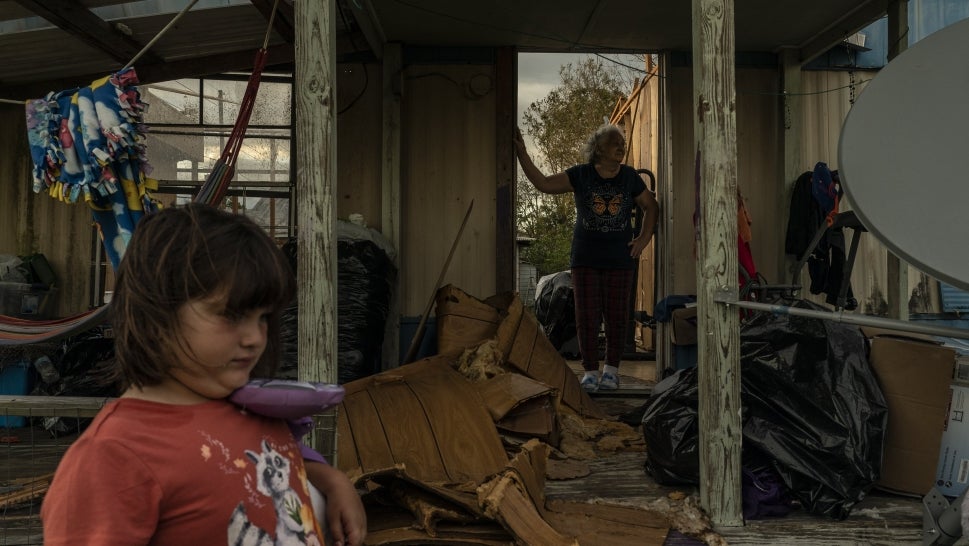 A child stands on the sidelines as her family surveys the damage to their home.