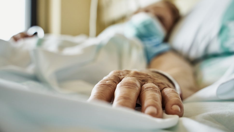 Blurred out body in mask with hand outstretched on a hospital bed
