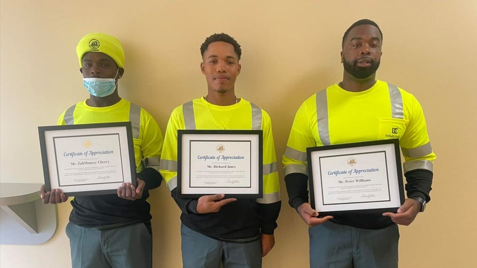 Three sanitation workers standing each holding certificates of appreciation