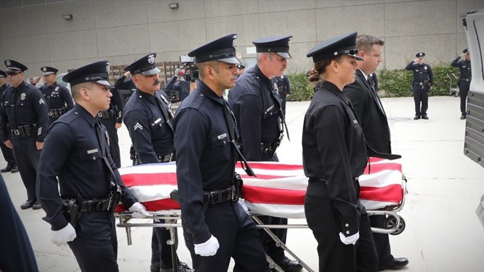 police officers standing around a body covered by the American Flag
