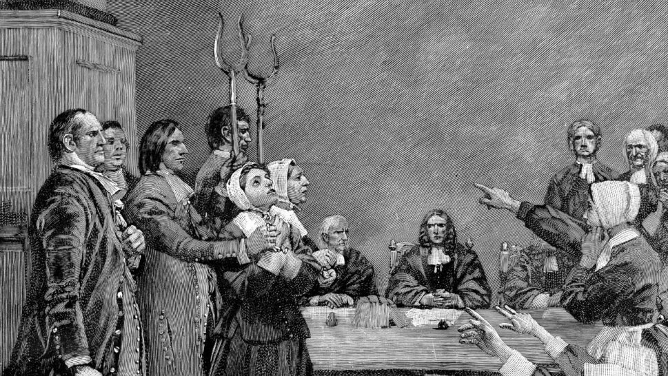 black and white drawing depicting a 17th century witch trial, woman holding her hands together looking at the sky, hold hold her from behind, other women point at her
