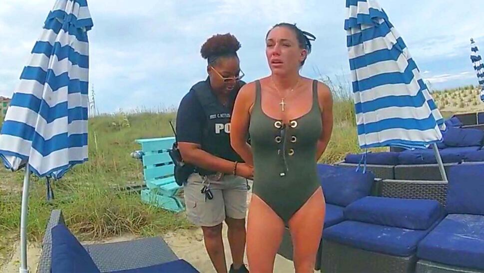 woman in green swimsuit being handcuffed by a police officer while on the beach.