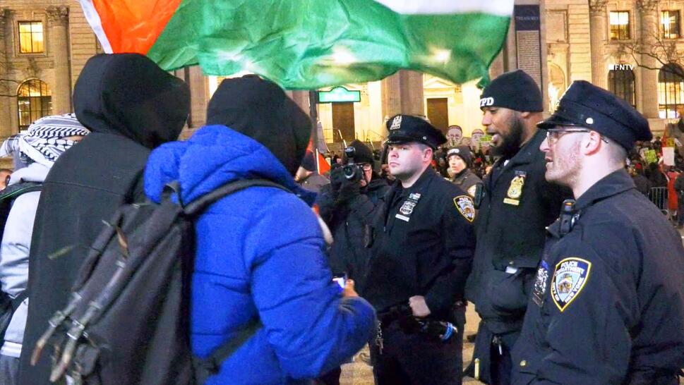 Three protestors holding a Palestine flag speaking with three New York police officers.