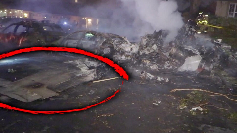 Photo of a plane crash's aftermath in a residential street. A red circle is around part of the crashed plane's wing.