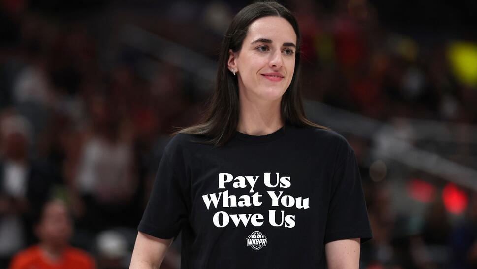 Caitlin Clark wears a shirt with the message "Pay Us What You Owe Us.