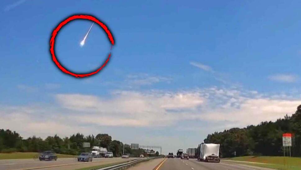 Dashcam view of a highway with a meteor falling from the sky, a red circle over the meteor 