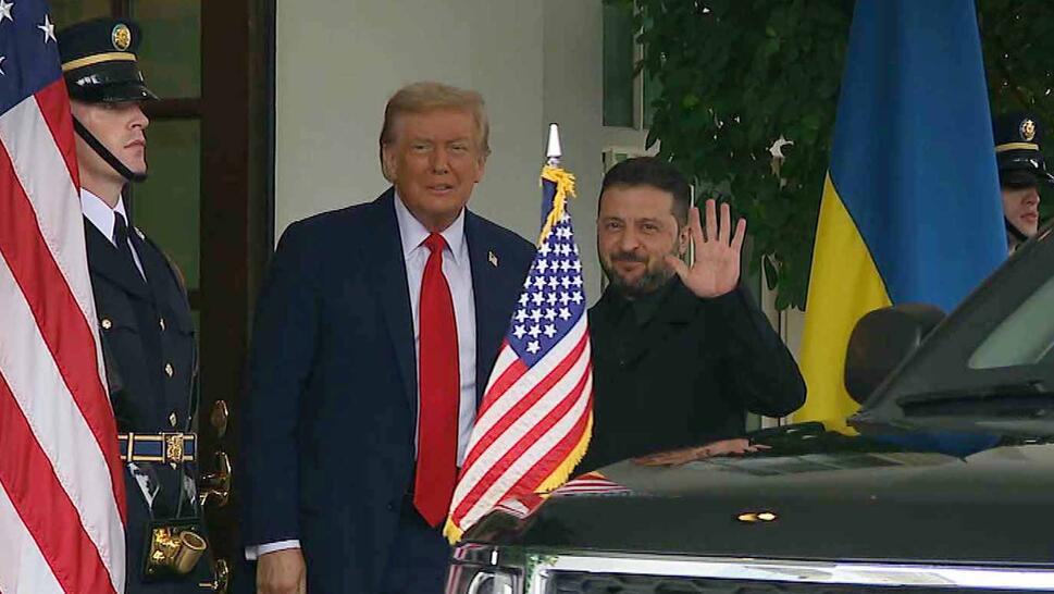 President Donald Trump standing next to President Zelenskyy outside the White House with an American flag in the foreground