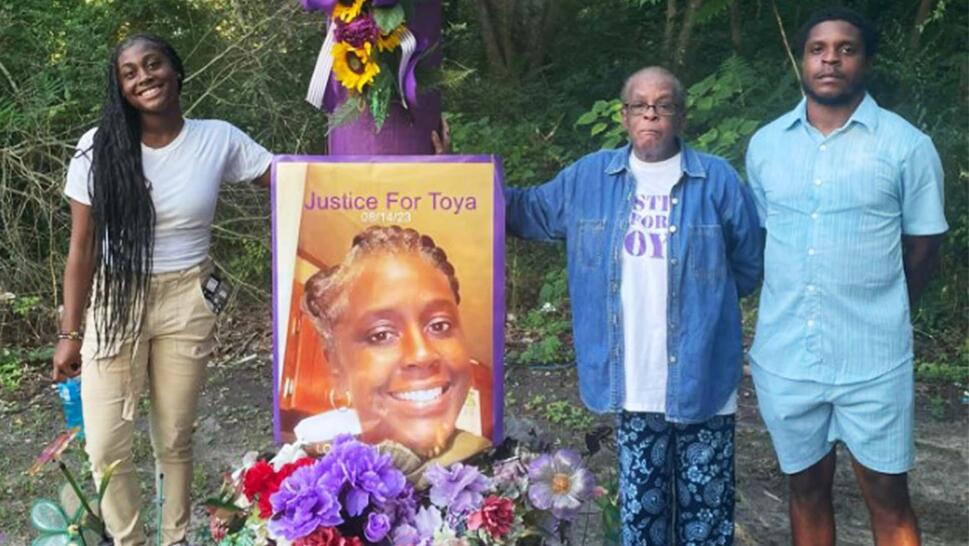 A family stands next to a memorial with a large sign reading 'Justice for Latoya'