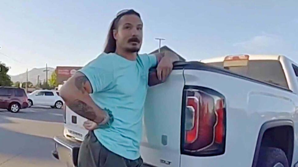 Travis Decker with his hand on his hip in a blue shirt leaning against a large white truck