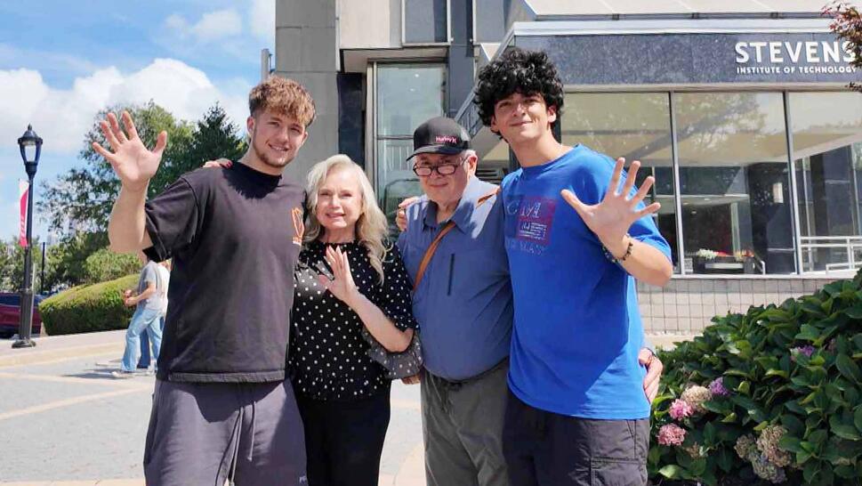 Family photo of two young adult men waiving next to an older man and woman 