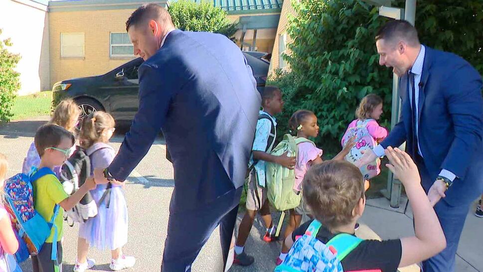 Child with a backpack fist bumps principal and navy blue suit / Child with a backpack high fives principal in navy blue suit