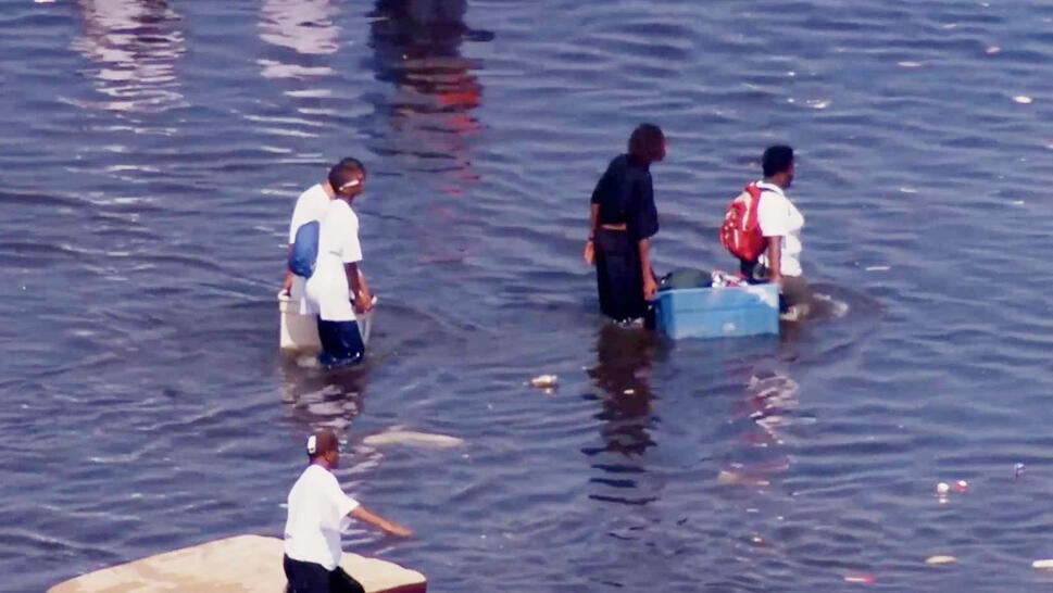 Residents walking in waist deep water carrying items as they evacuate 