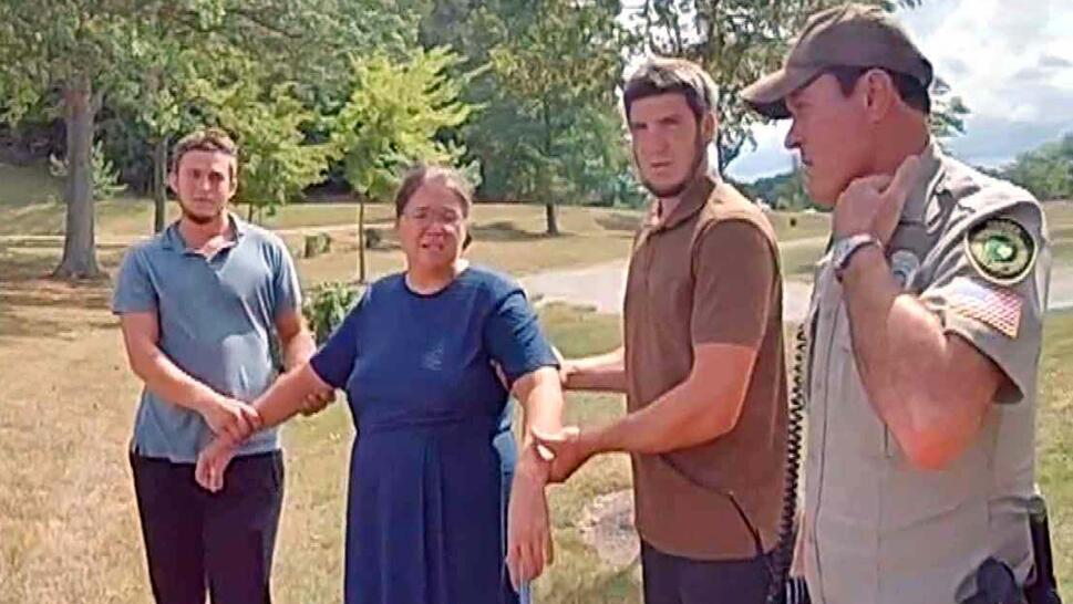Two men holding onto a woman's arms next to a sheriff's deputy.