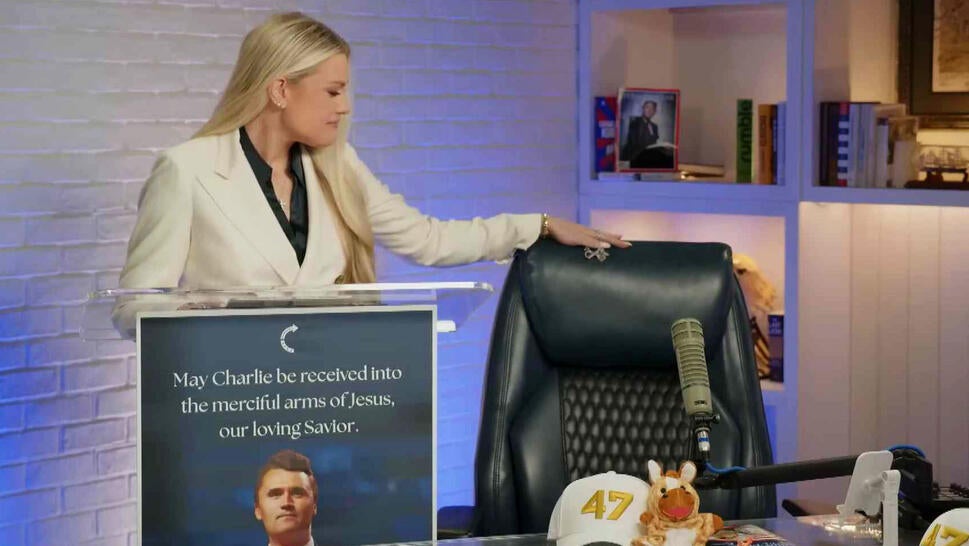 Charlie Kirk's wife speaking behind a podium with her hand on the chair Kirk recorded his podcast from