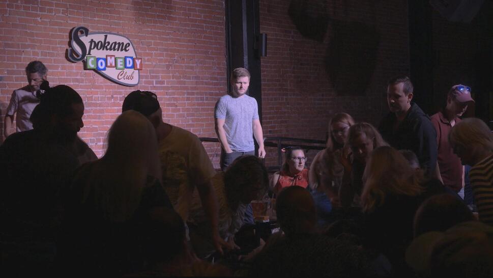 Comedian Drew Lynch watches from the stage as an audience member needs assistance